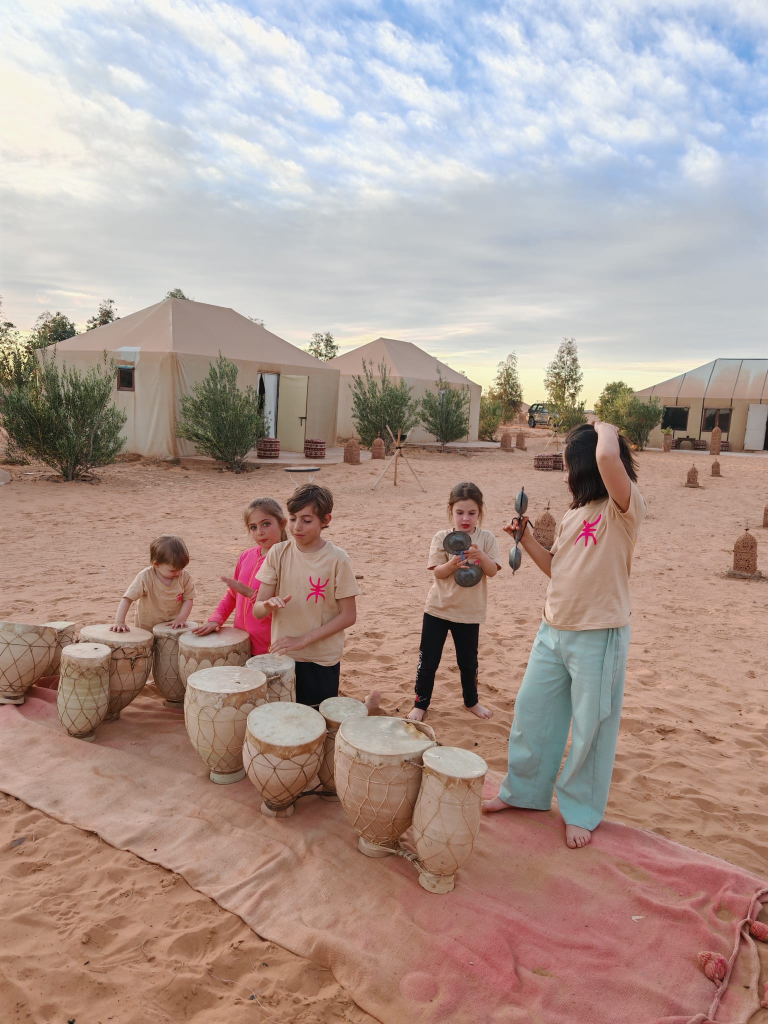 Niños tocando tambores en la arena frente a las jaimas de un campamento en Merzouga