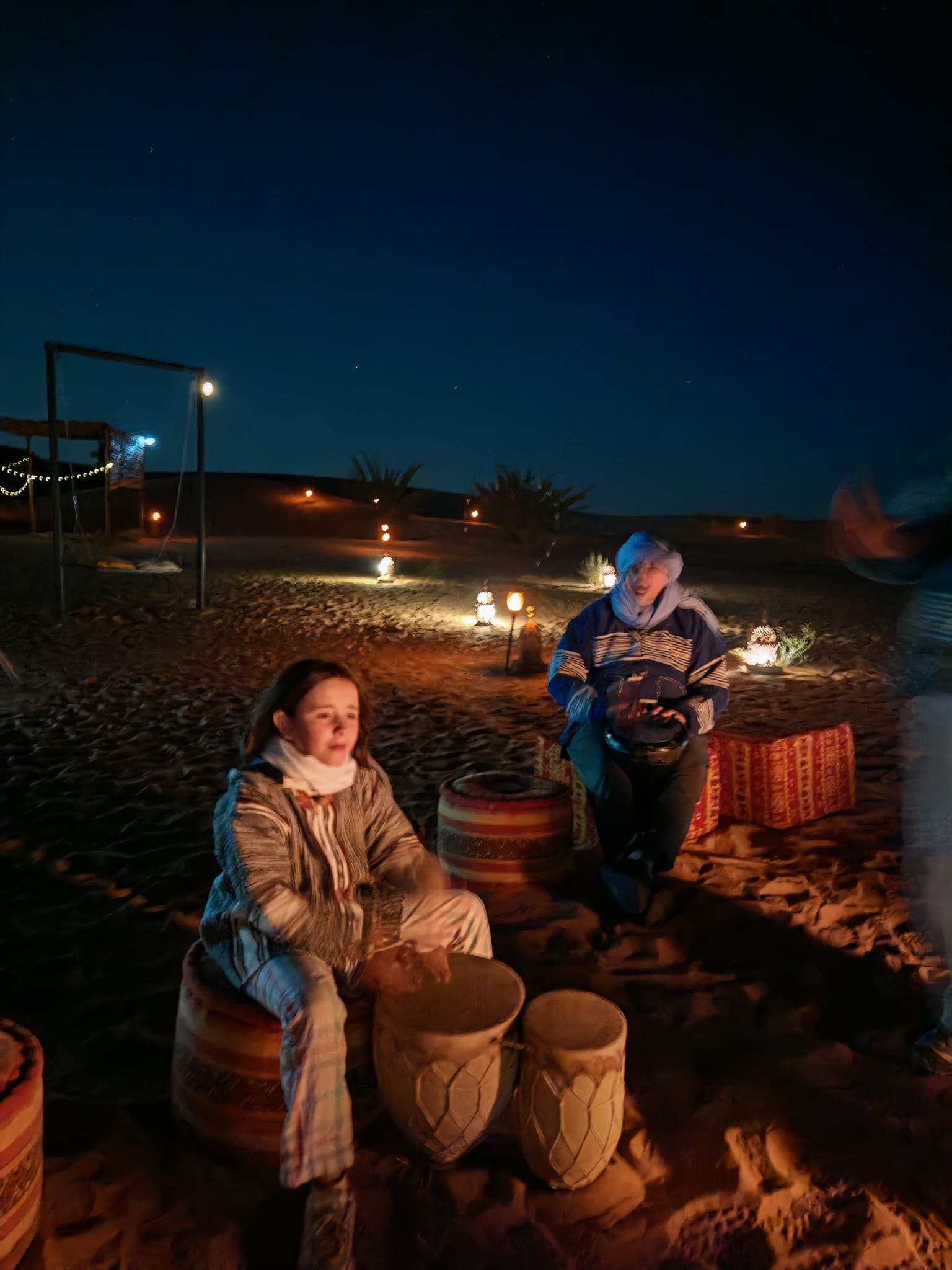 Niña tocando tambores bereberes de noche en un campamento del desierto de Merzouga